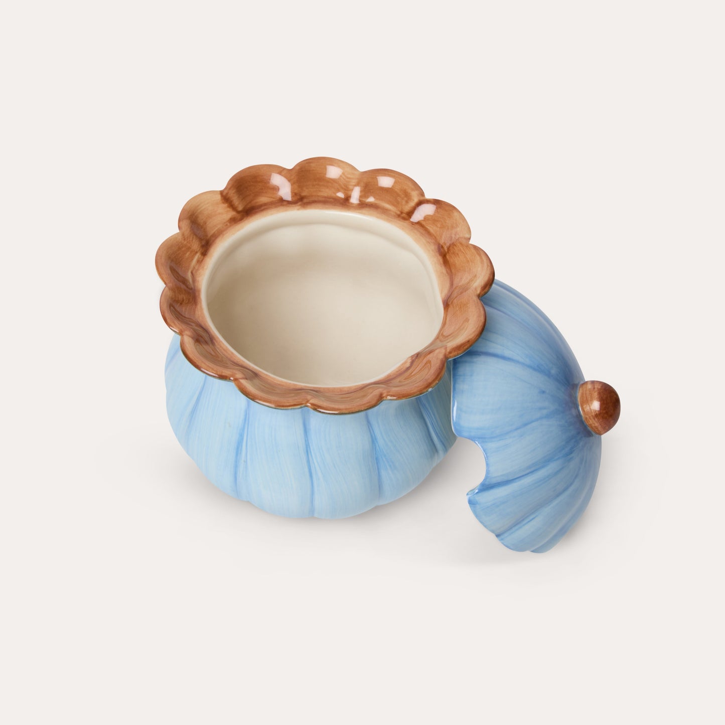 A decorative ceramic pumpkin-shaped container with a matching lid, featuring a light blue body, a brown scalloped rim, and a cream-colored interior, set against a plain off-white background.