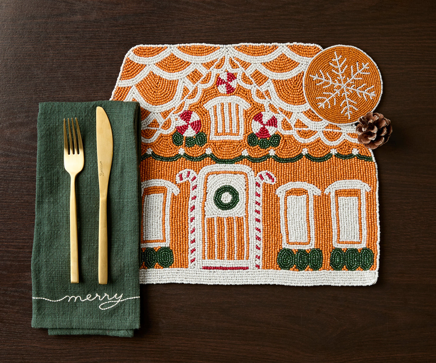 Gingerbread house beaded placemat with gold flatware, a green napkin and a beaded snowflake coaster