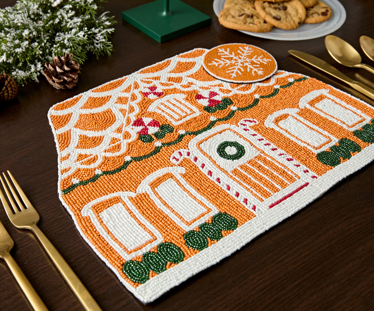Gingerbread house beaded placemat beside a beaded snowflake coaster on a dark wood table
