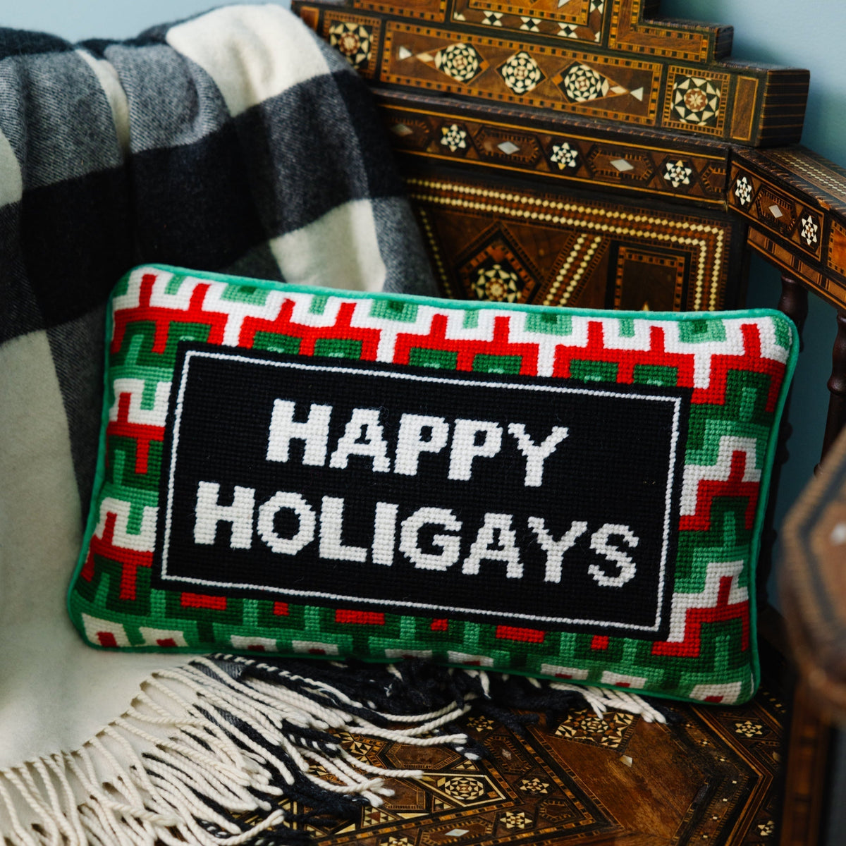 Decorative pillow with 'Happy Holigays' text on a wooden surface with a blanket and decorative box.