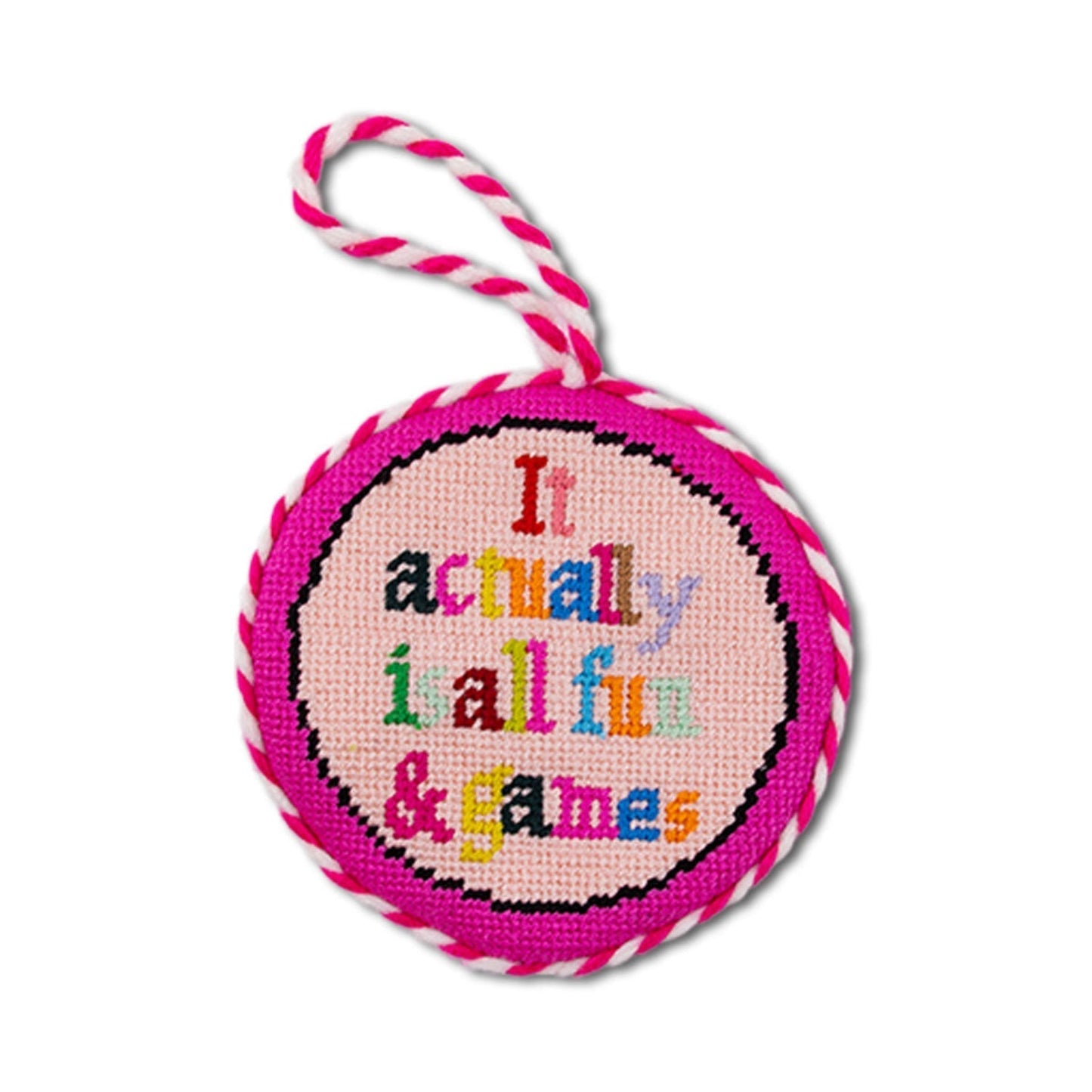Round pink needlepoint ornament with colorful text and striped string on a white background
