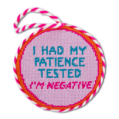 Round pink needlepoint tag with text 'I had my patience tested, I'm negative' on a white background
