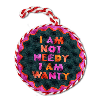 Round needlepoint ornament with colorful text and braided handle on a white background