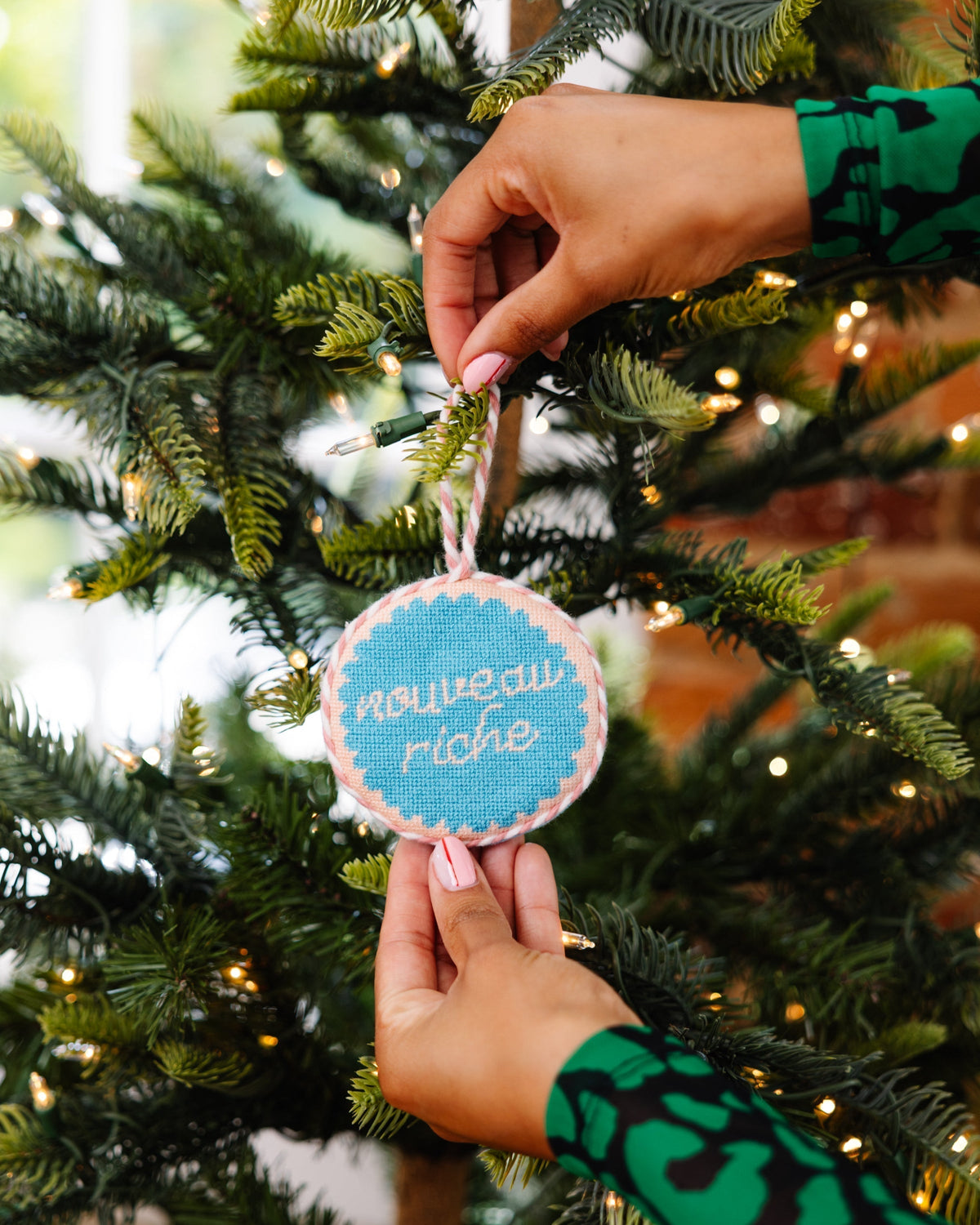 Person hanging a Christmas ornament on a tree with blurred lights in the background
