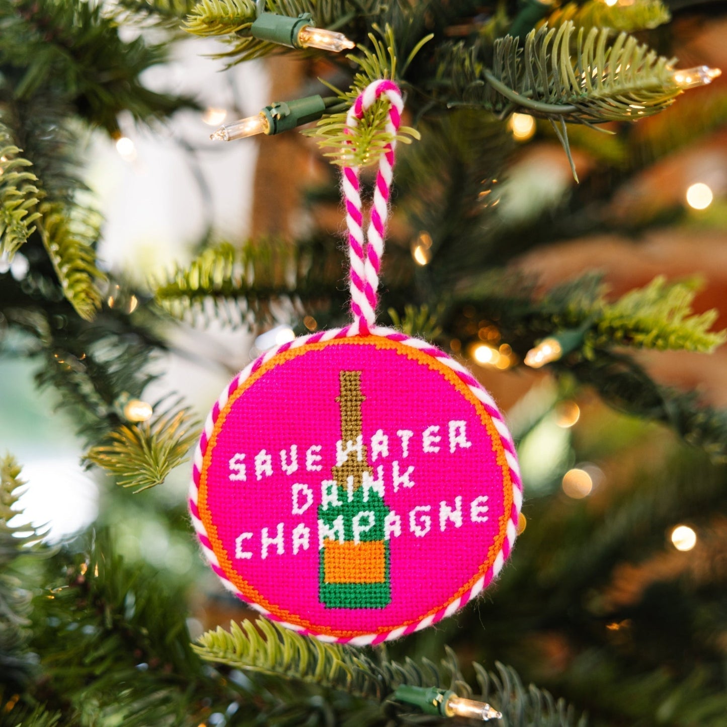 Decorative ornament with 'Save Water, Drink Champagne' text on a Christmas tree.