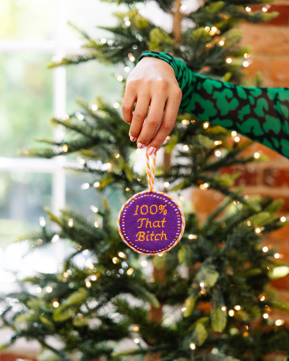 Hand holding a Christmas ornament with text in front of a decorated tree