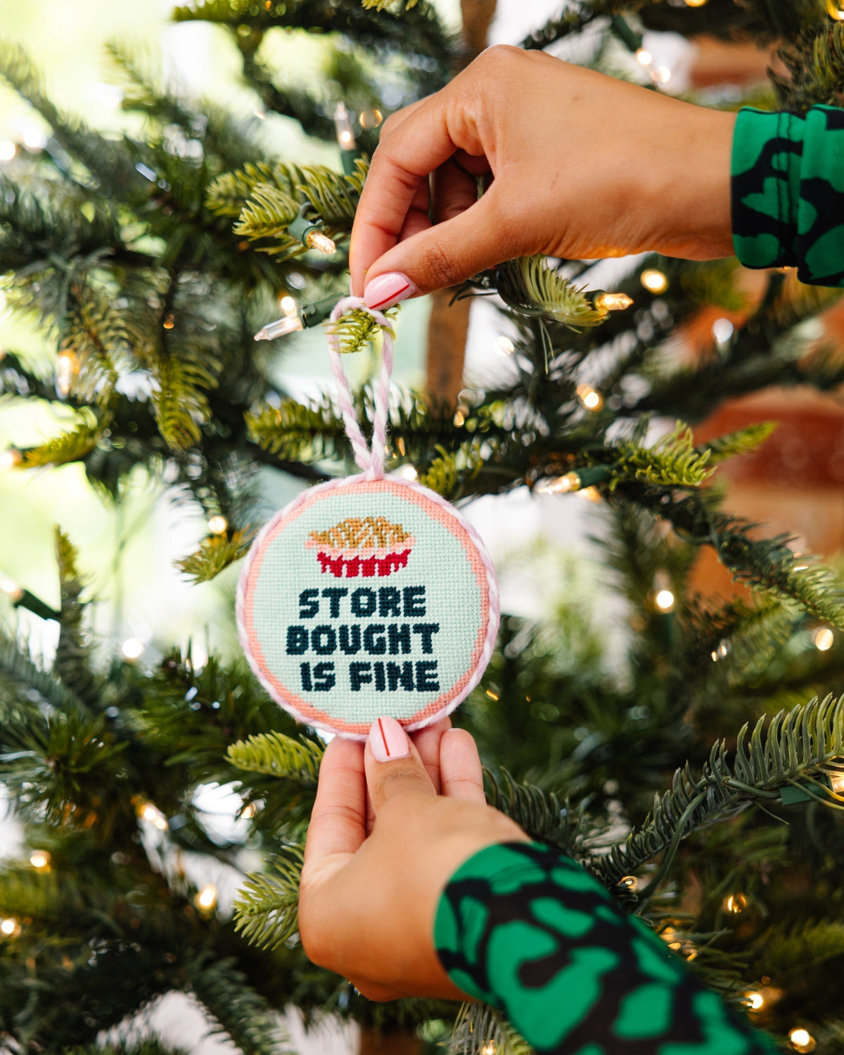 Person decorating a Christmas tree with a humorous ornament