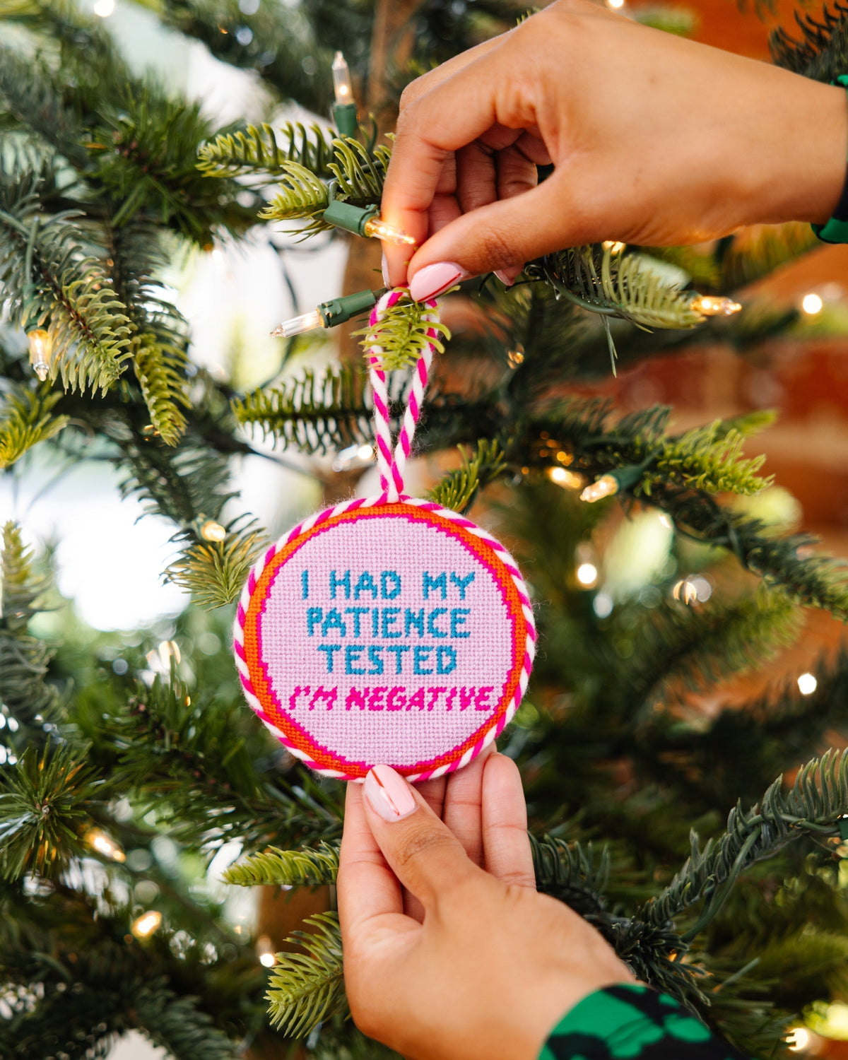 Person holding a Christmas ornament with text on a decorated tree
