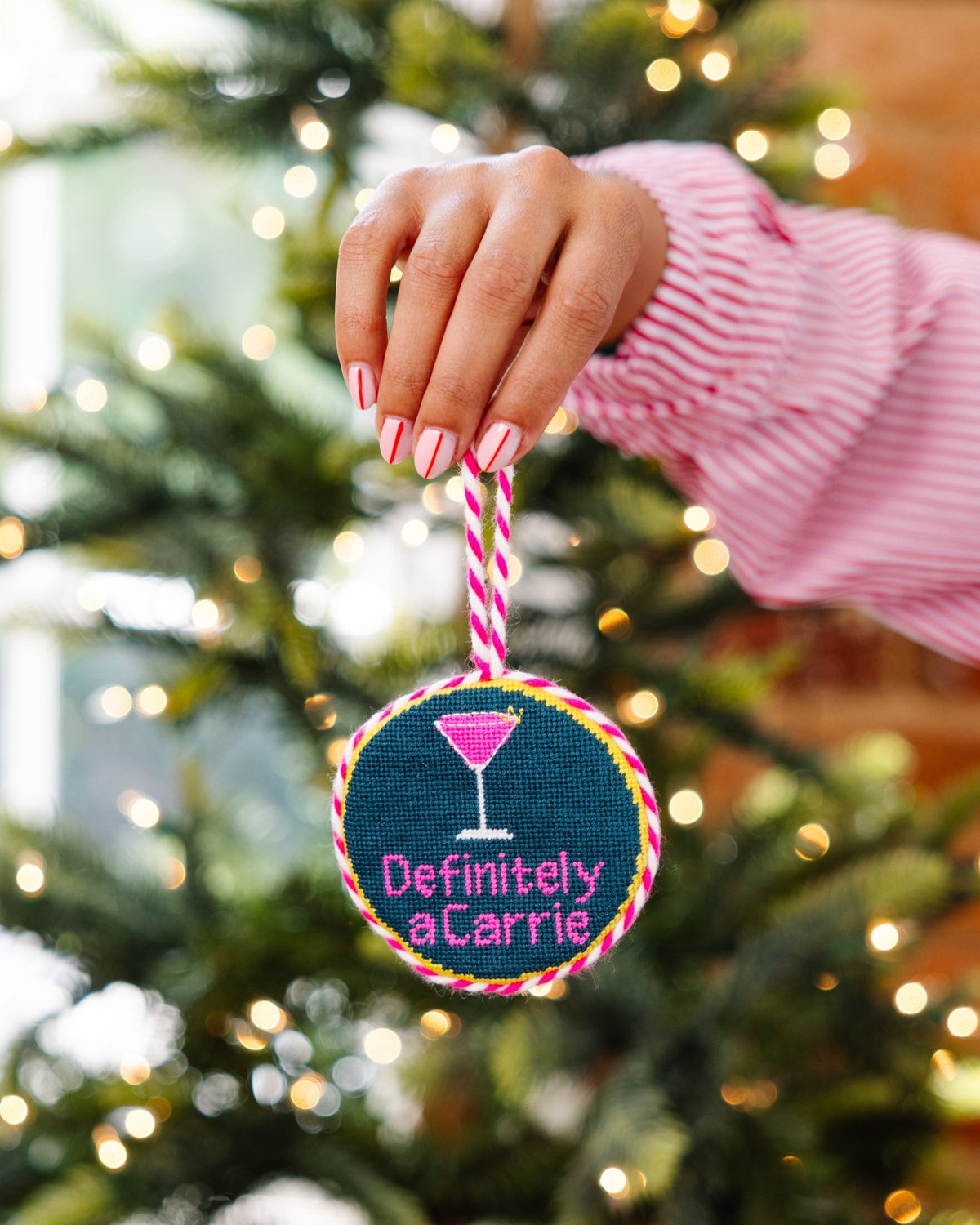 Hand holding a decorative ornament with 'Definitely a Carrie' text against a Christmas tree background