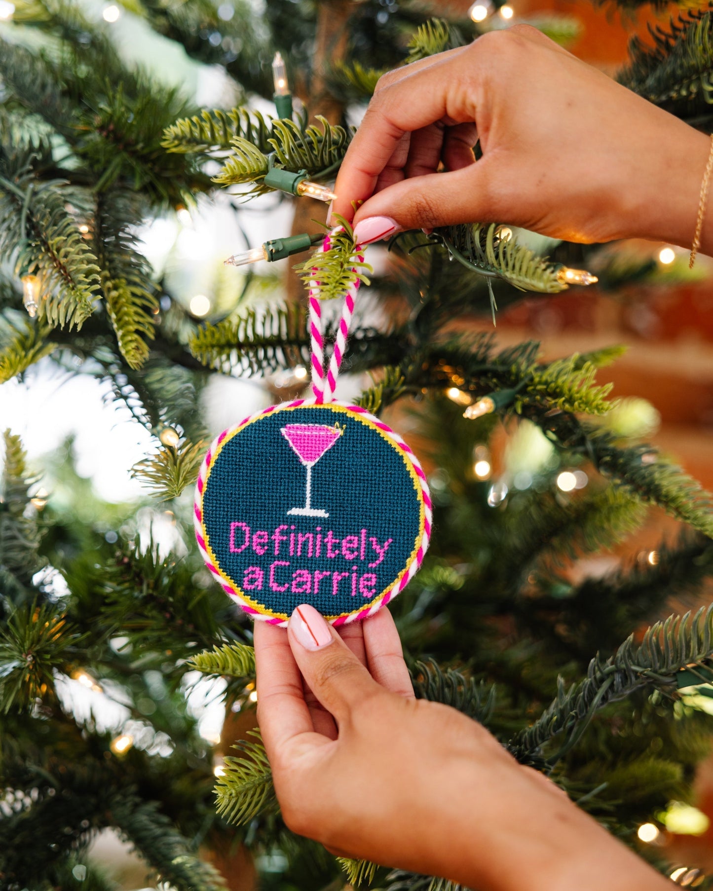 Hand holding a Christmas ornament with 'Definitely a Carrie' text against a decorated tree background