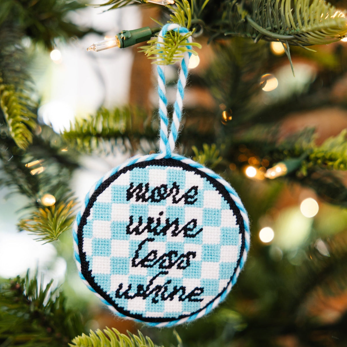 Decorative ornament with 'more wine less wine' text on a Christmas tree.