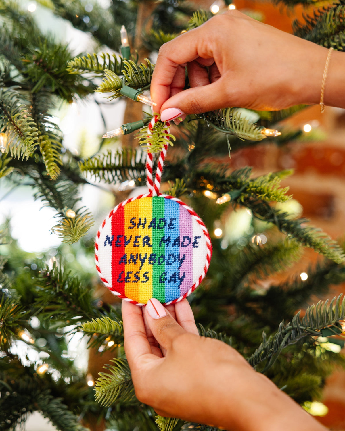 Hand holding a rainbow-colored ornament with text on a Christmas tree