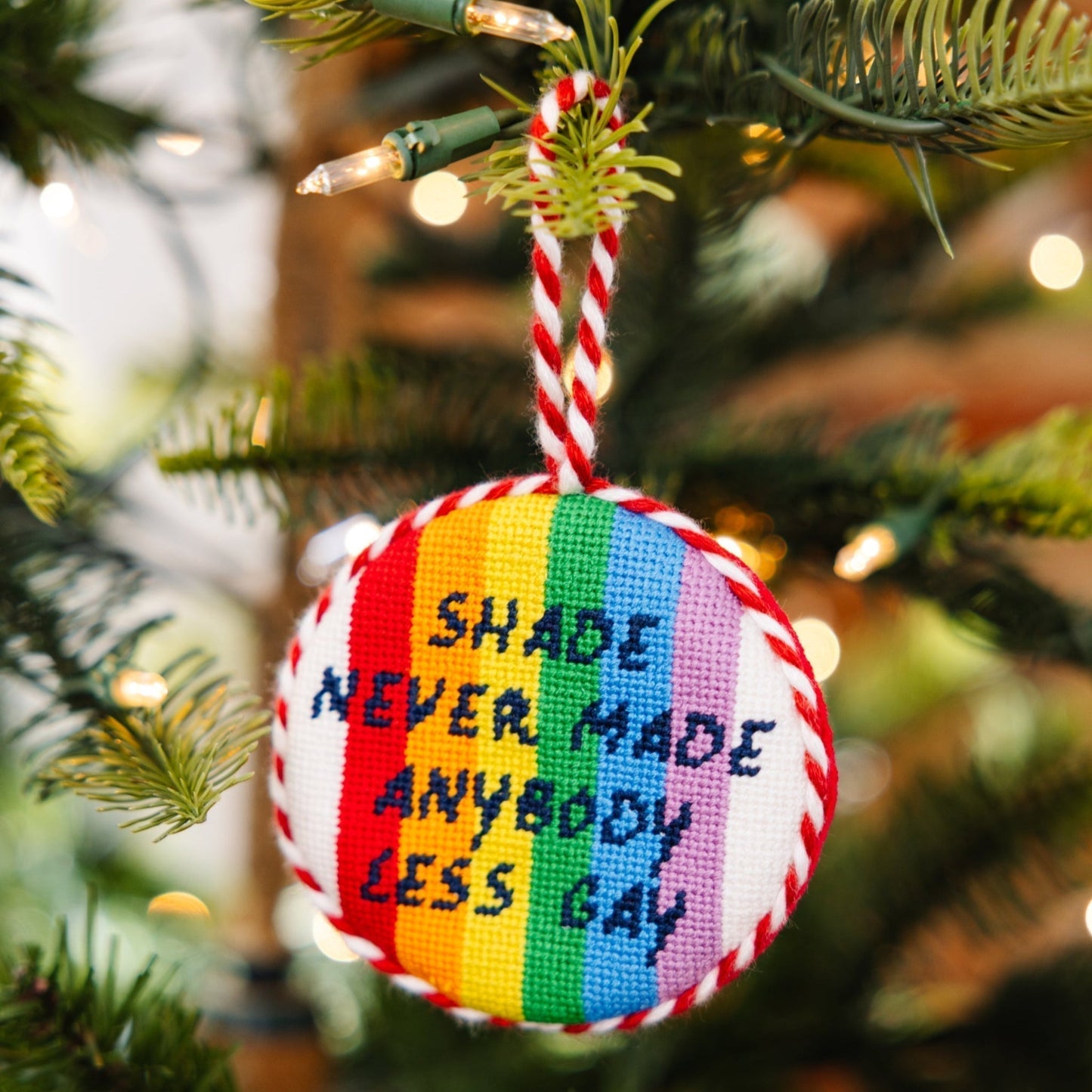 Decorative ornament with rainbow design and text hanging on a Christmas tree.
