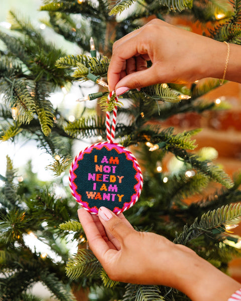 Hand holding a Christmas ornament with text on a decorated tree