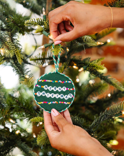 Hand holding a festive ornament with 'Merry Swiffermas' text on a decorated Christmas tree.