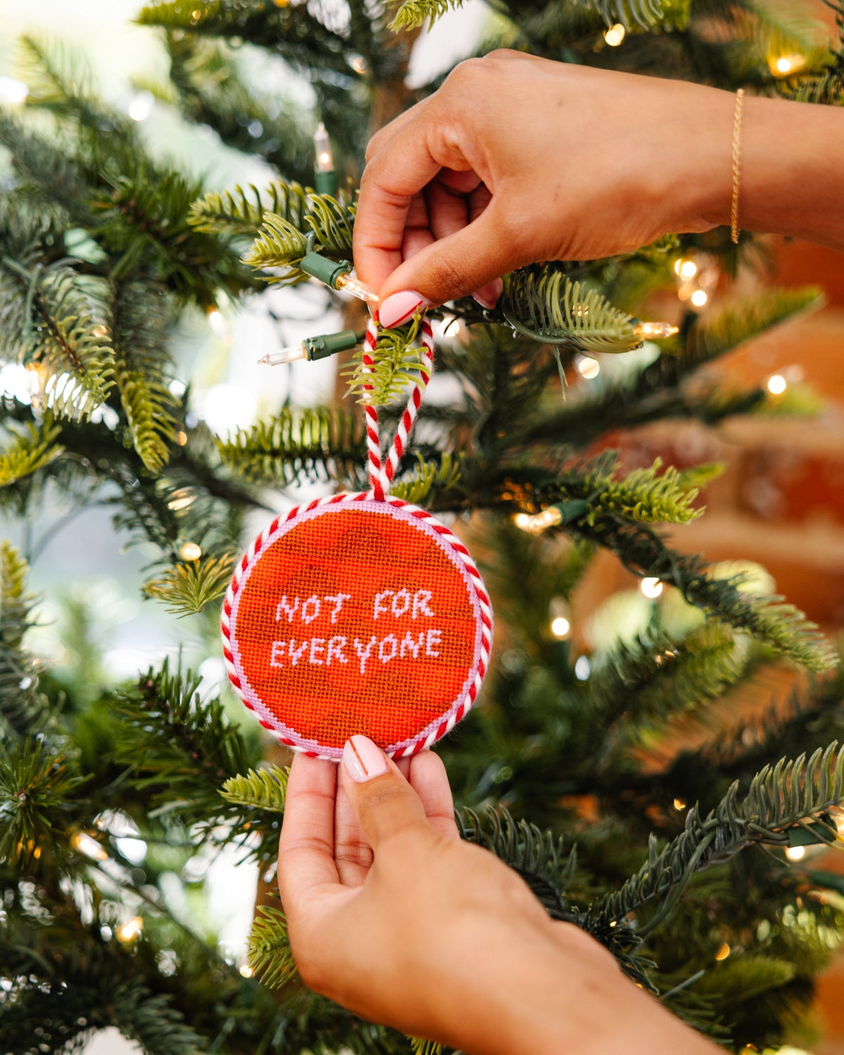 Hand holding a red ornament with 'Not for Everyone' text on a decorated Christmas tree.