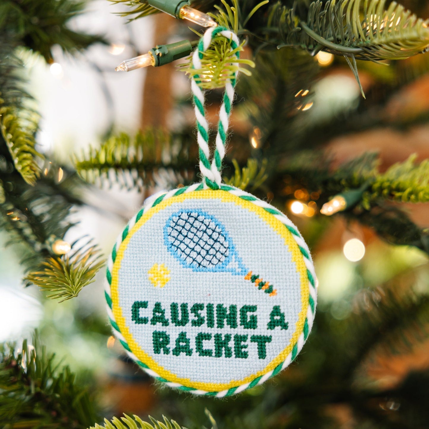 Decorative ornament with 'Causing a Racket' text and racquet design on a Christmas tree.