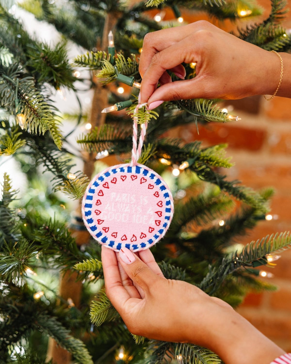 Hand holding a decorative ornament in front of a Christmas tree.