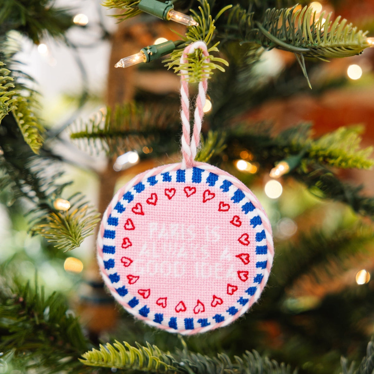 Decorative ornament with pink and blue pattern hanging on a Christmas tree.