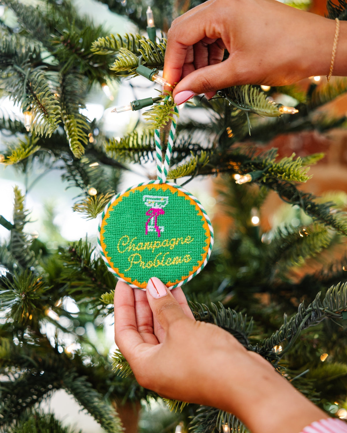 Hand placing a Christmas ornament with 'Champagne Problems' text on a tree.