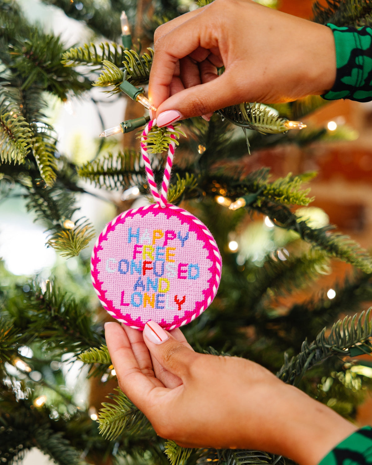 Hand holding a Christmas ornament with colorful text against a festive tree background