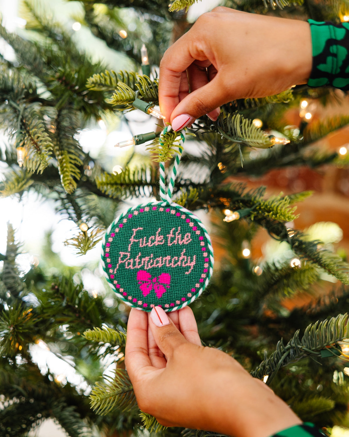 Person holding a Christmas ornament with text on a decorated tree