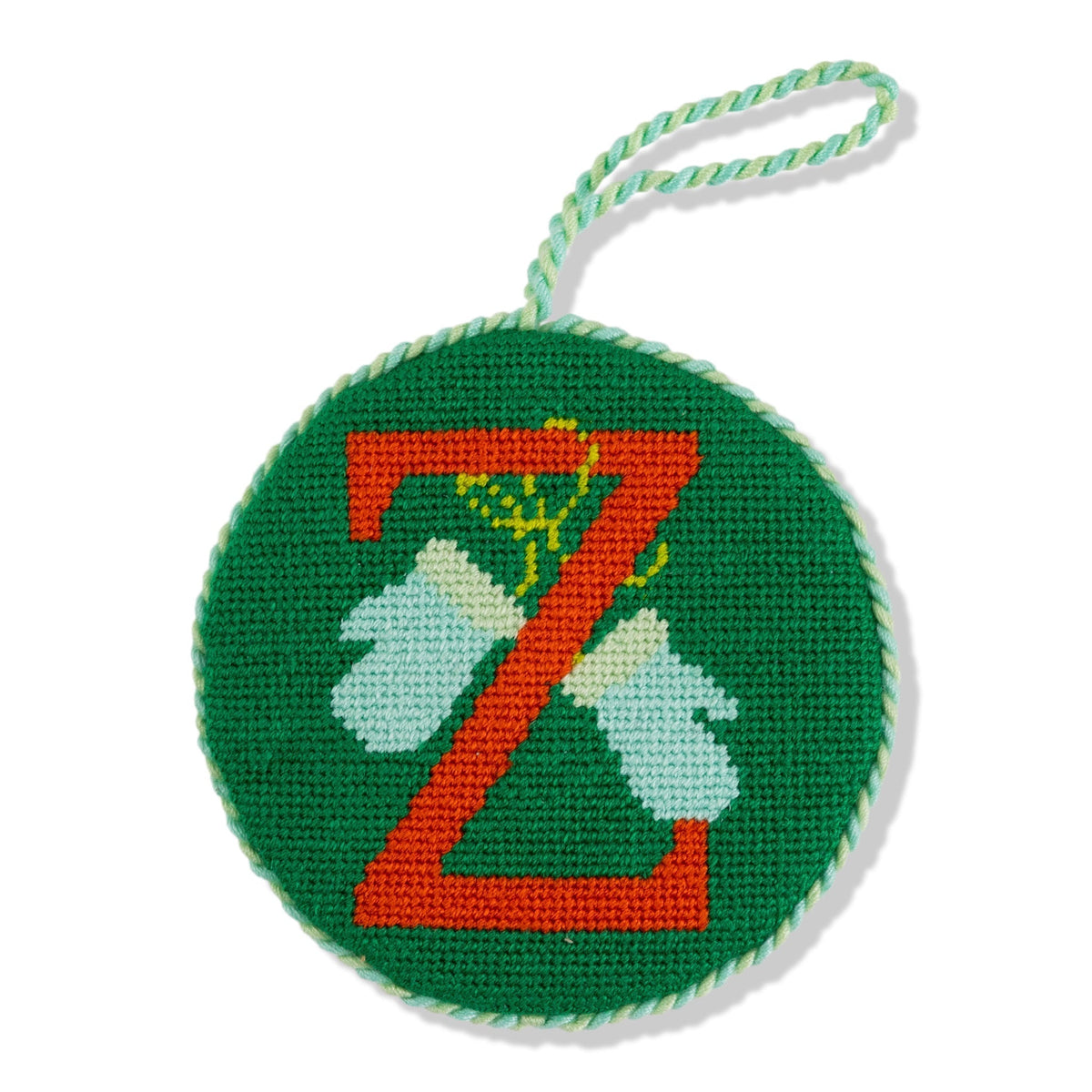 Circular green needlepoint ornament with orange 'Z' design on a white background