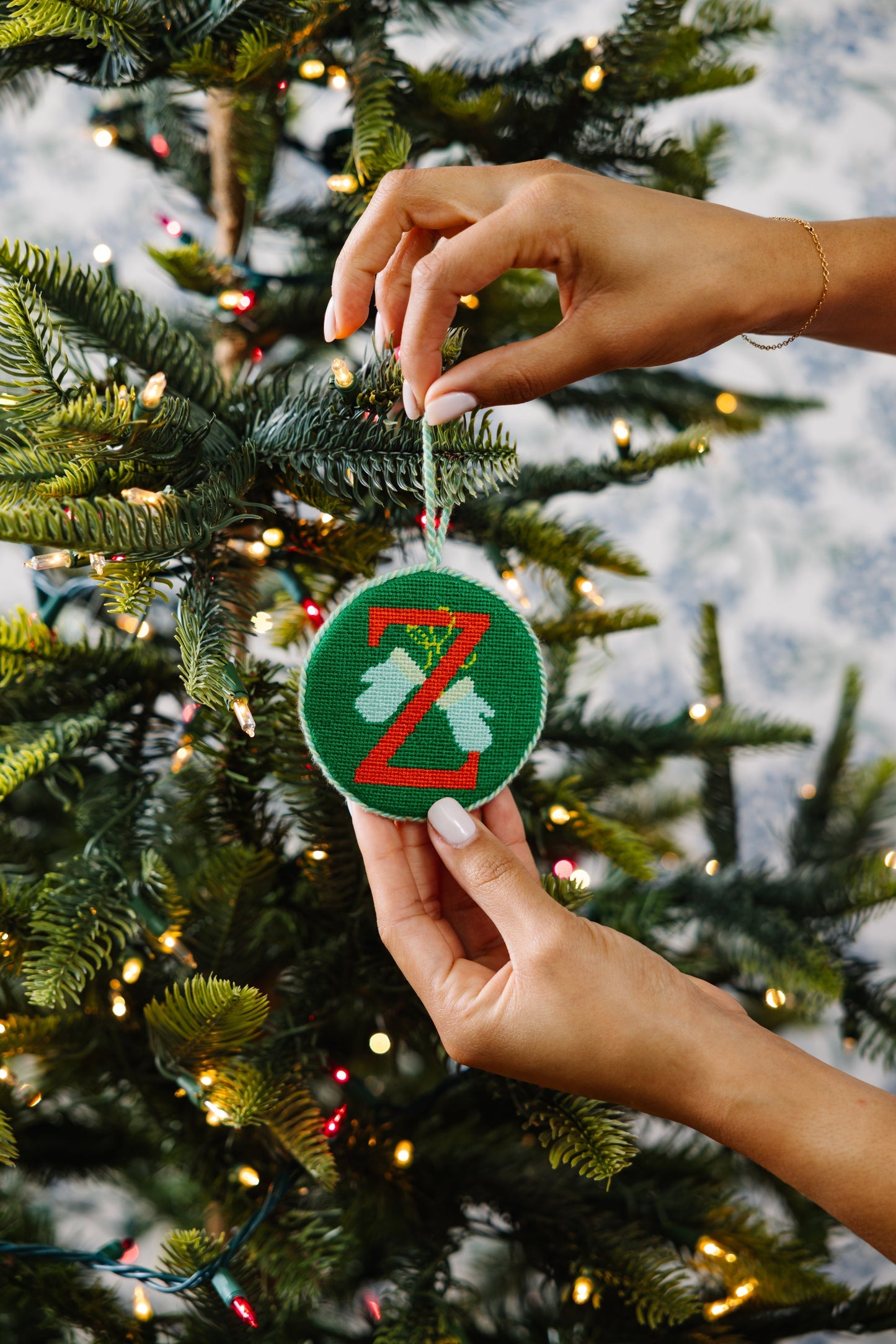 Hand holding a green ornament with a red 'Z' in front of a decorated Christmas tree.