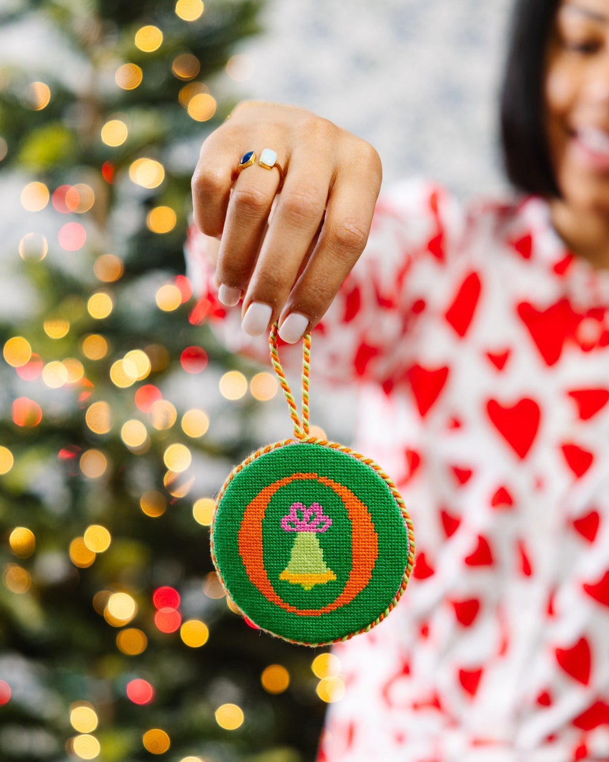 Person holding a Christmas ornament with a blurred Christmas tree in the background