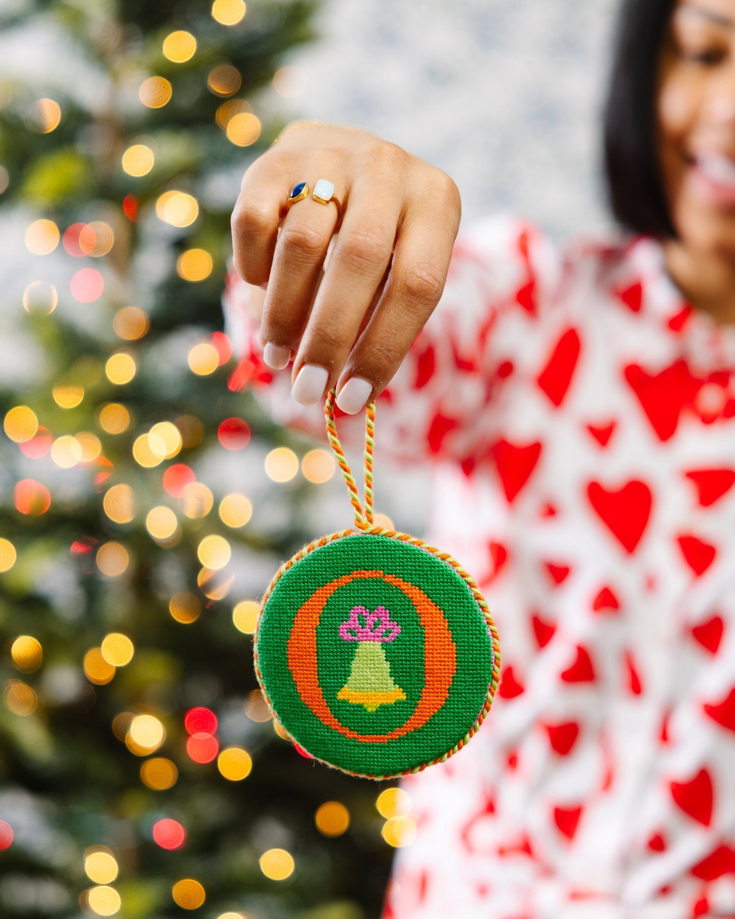 Person holding a Christmas ornament with a blurred Christmas tree in the background