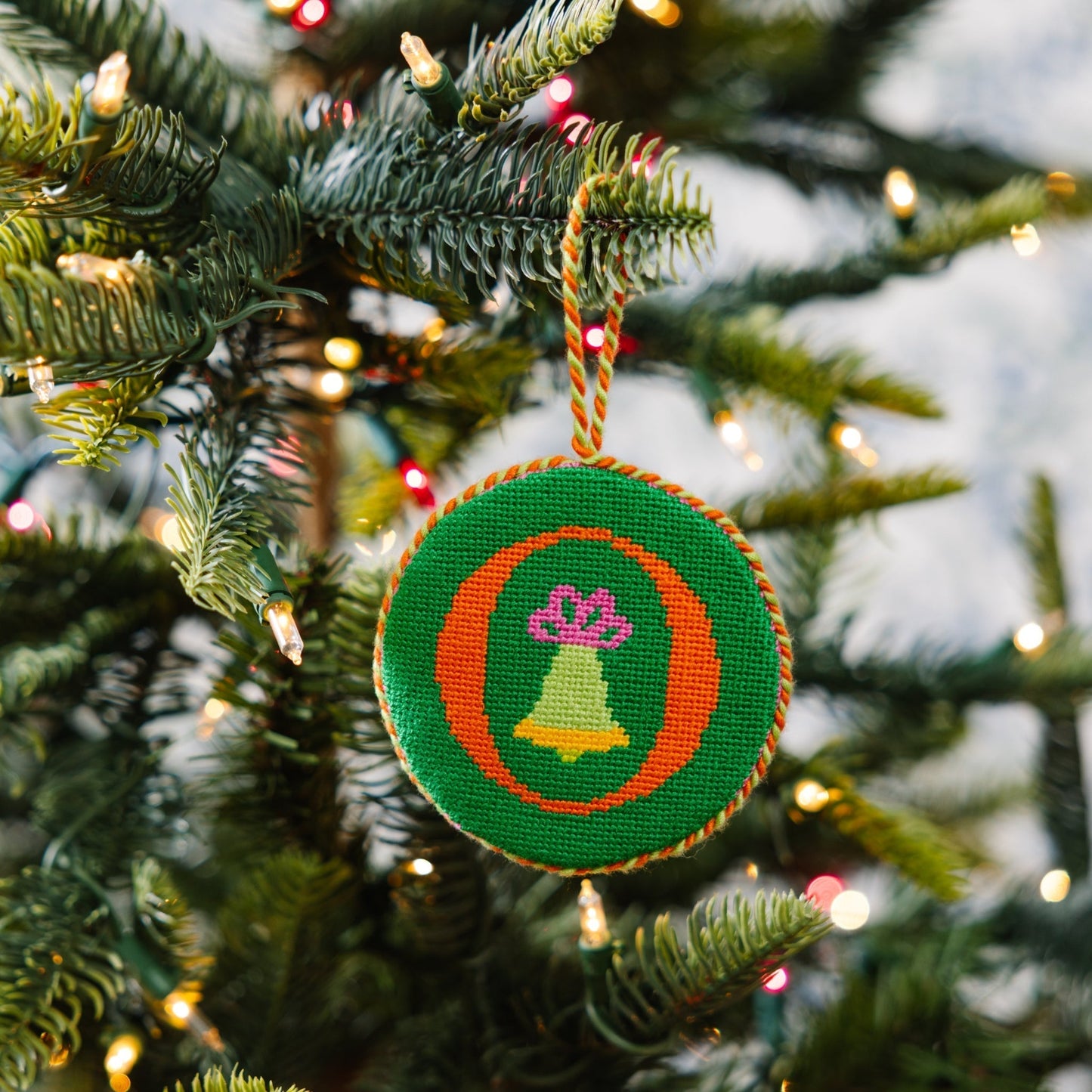 Decorative Christmas ornament with a green circle and bell design on a Christmas tree.