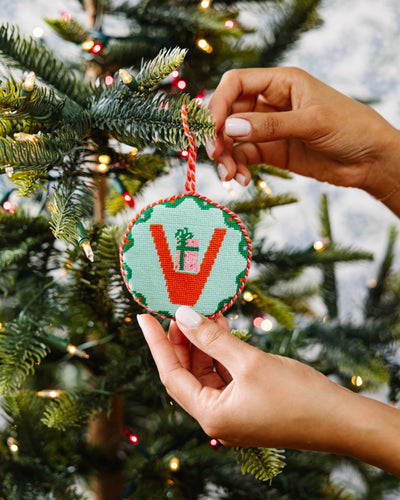 Hand holding a decorative ornament in front of a Christmas tree