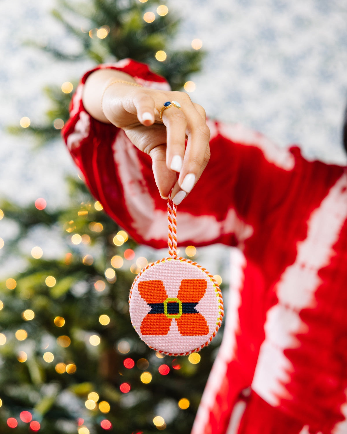 Person wearing a red sweater holding a Christmas ornament with a tree in the background