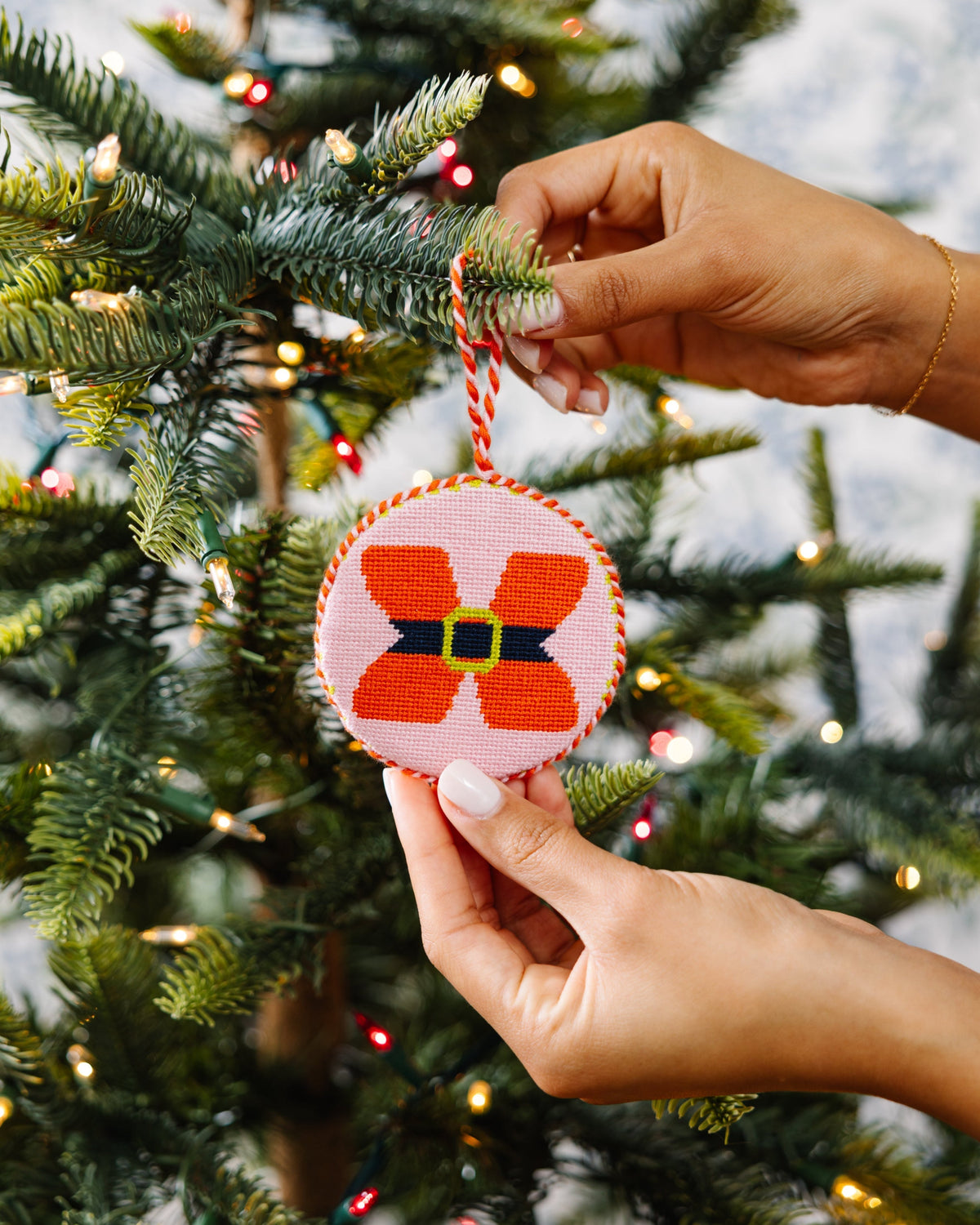Hand holding a decorative ornament with a butterfly design against a Christmas tree background.