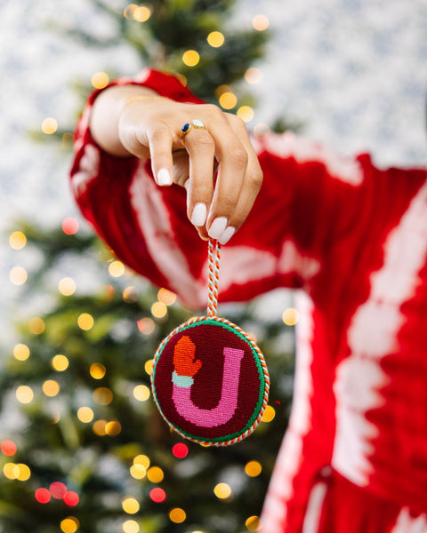 Person wearing a red sweater holding a Christmas ornament with a letter 'J' in front of a decorated tree.