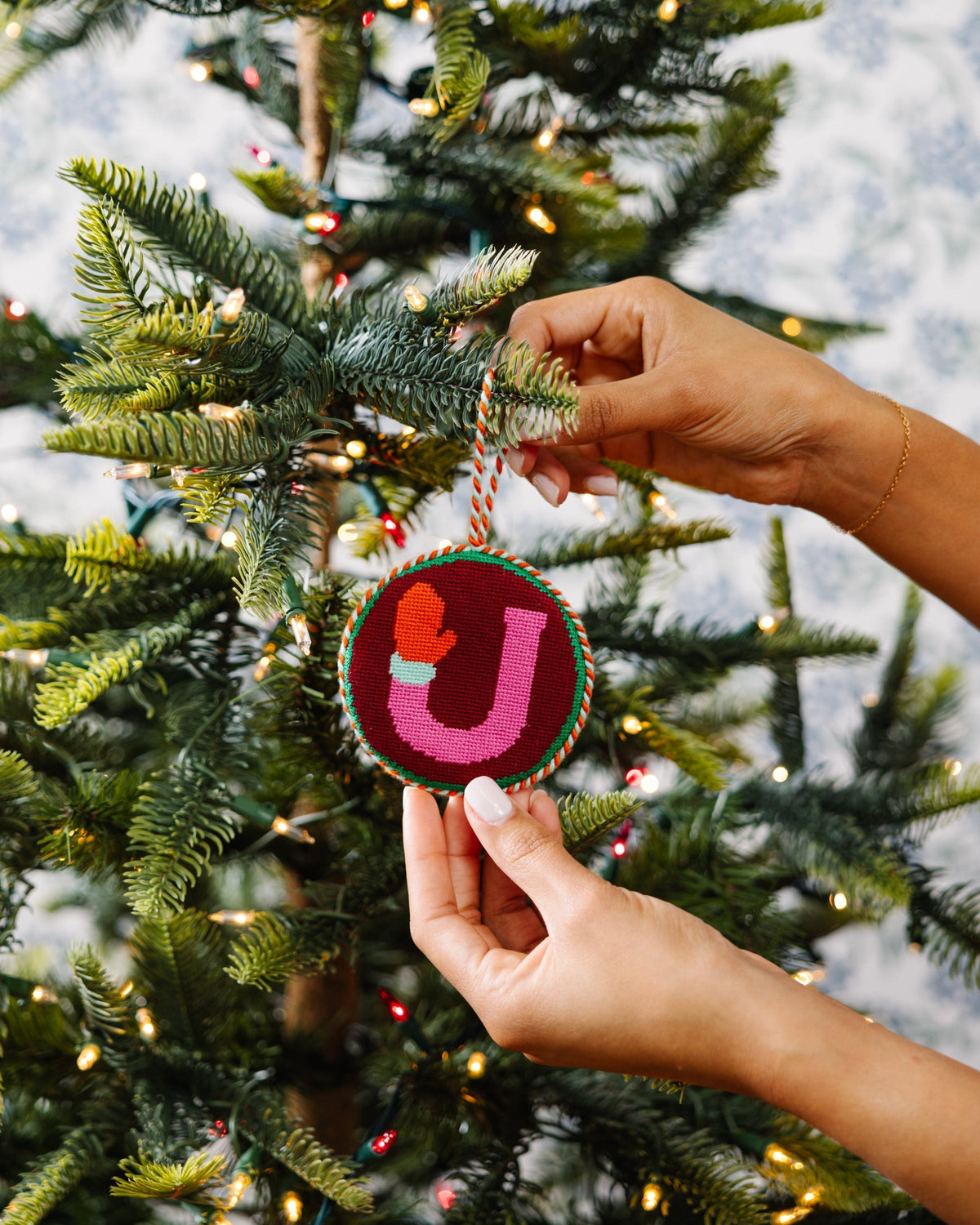 Person hanging a decorative ornament with a heart and letter 'J' on a Christmas tree.