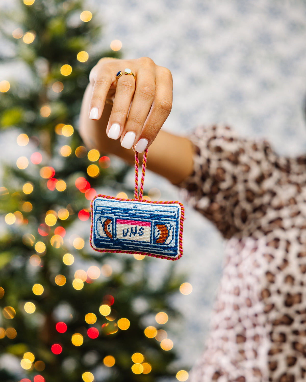 Person holding a VHS tape ornament in front of a decorated Christmas tree.