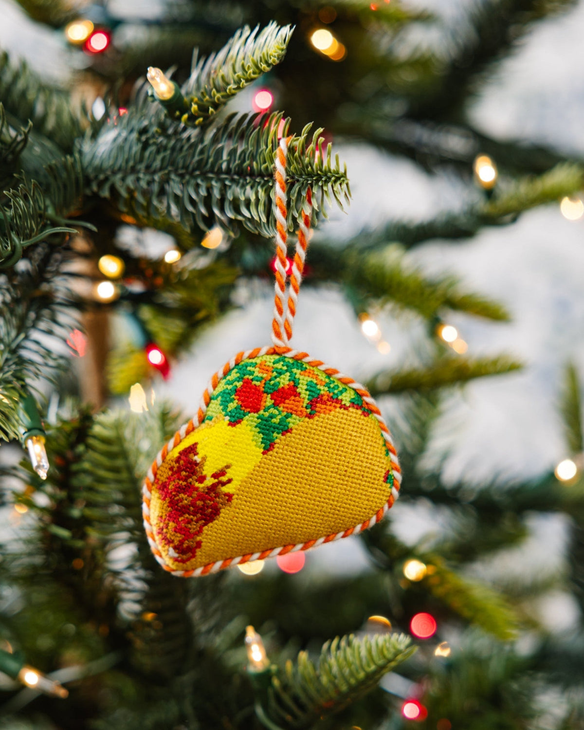Decorative taco ornament on a Christmas tree with lights in the background