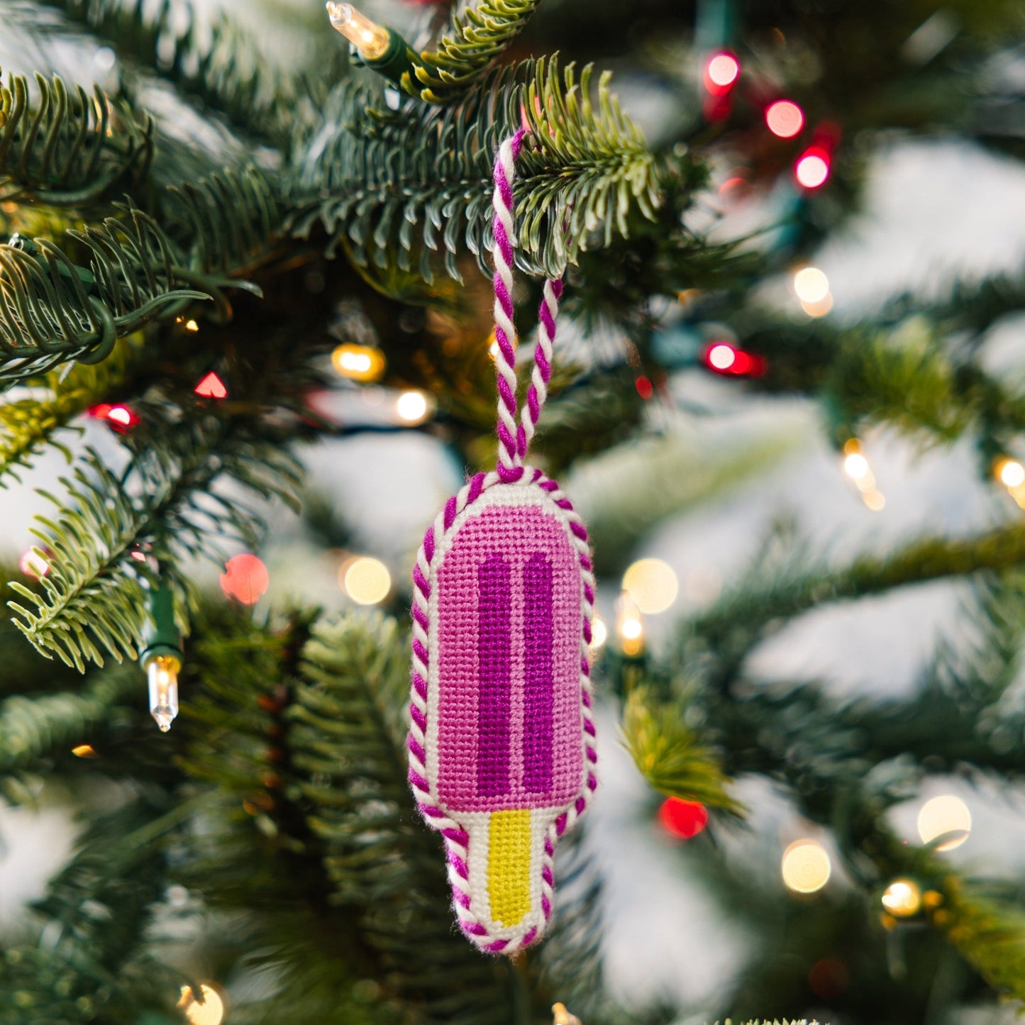 Decorative ice cream popsicle ornament on a Christmas tree with lights in the background