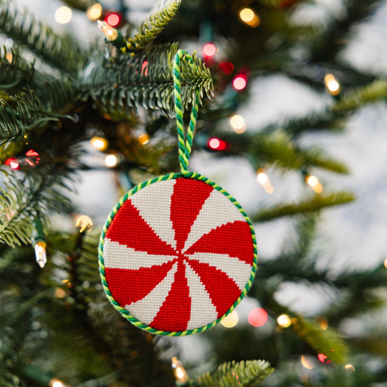 Red and white peppermint candy ornament on a Christmas tree with lights.