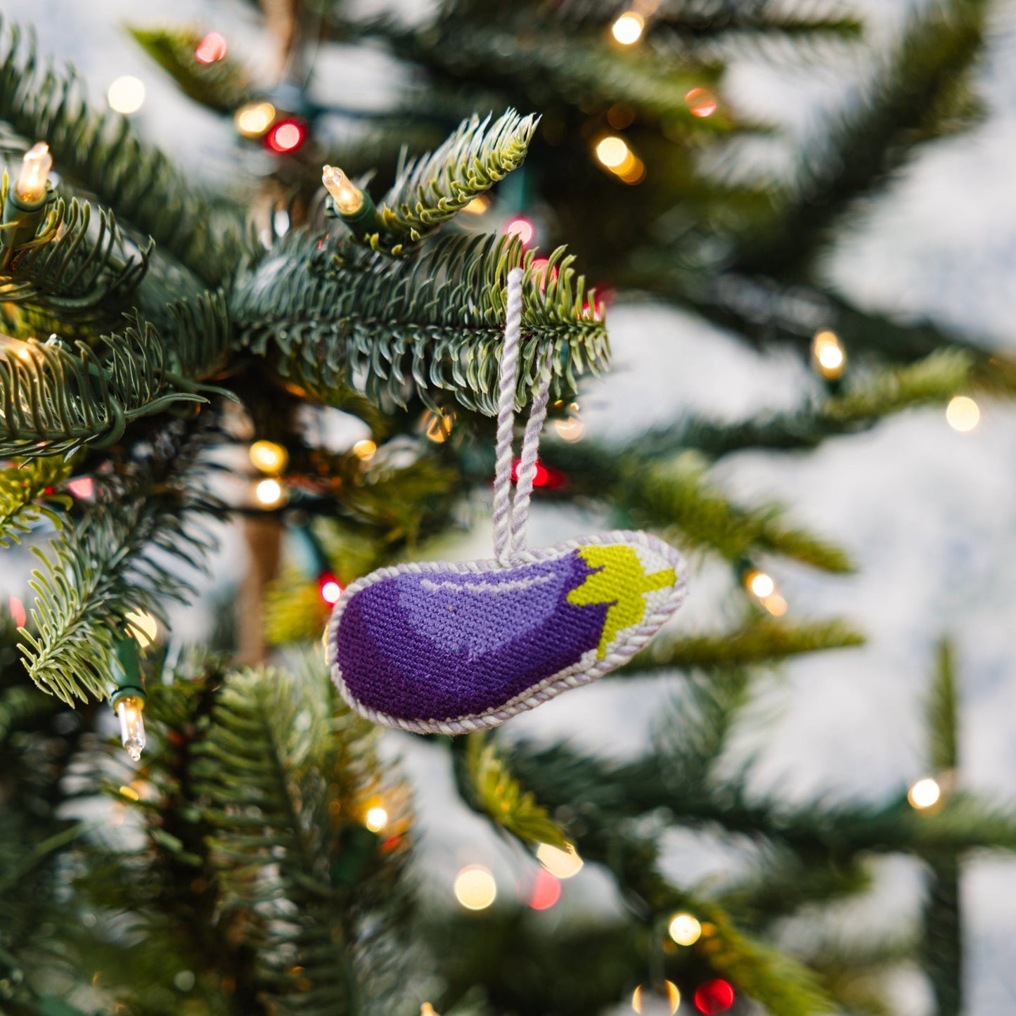 Decorative eggplant ornament on a Christmas tree with lights.