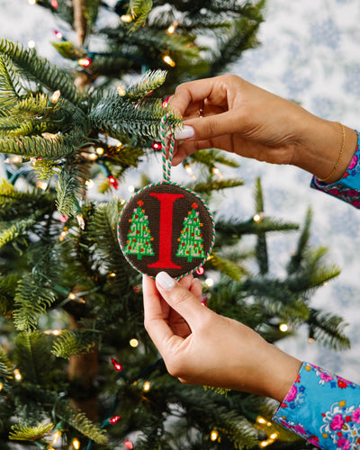 Person decorating a Christmas tree with a ornament featuring the letter 'I'.