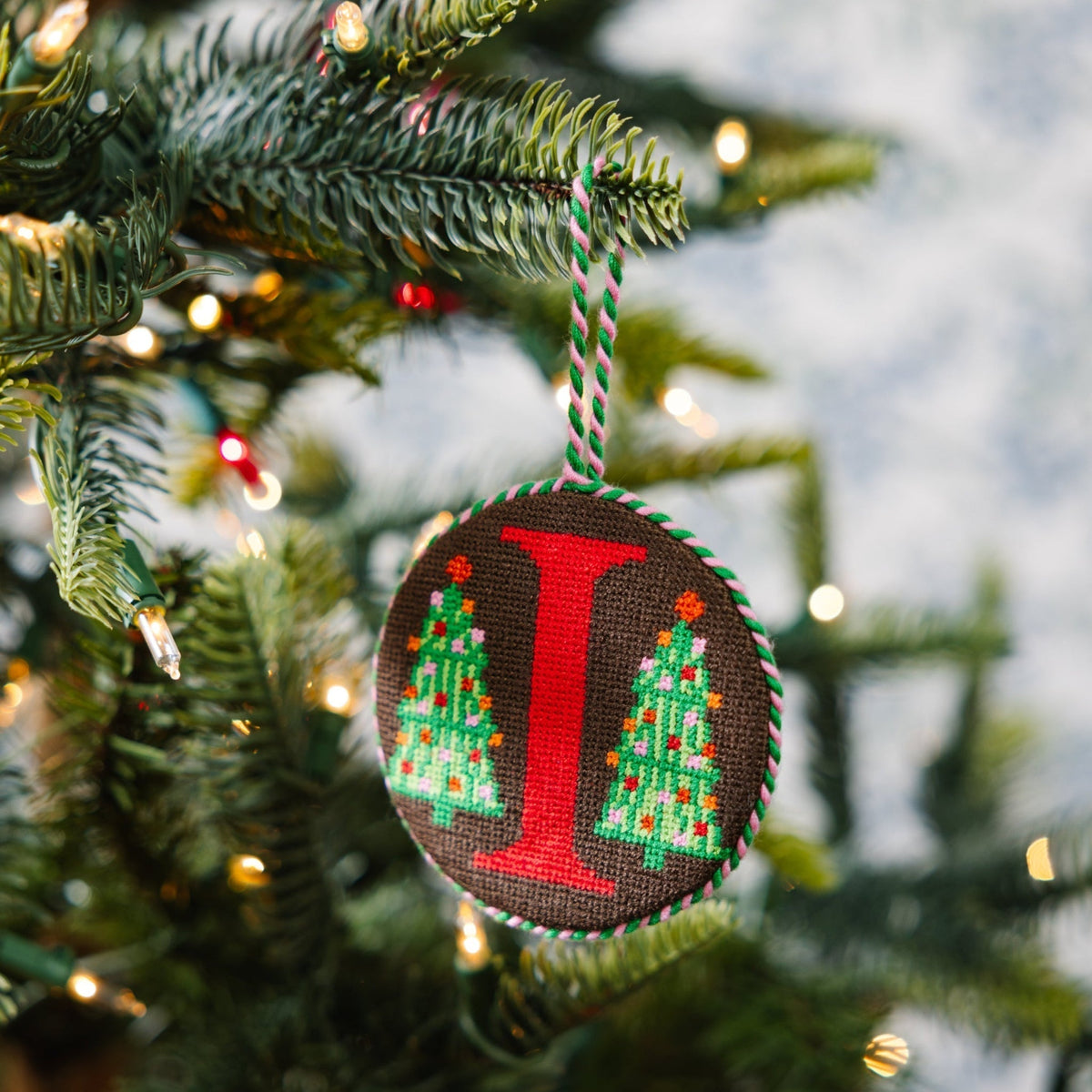 Decorative Christmas ornament with letter 'I' and Christmas tree design hanging on a tree.