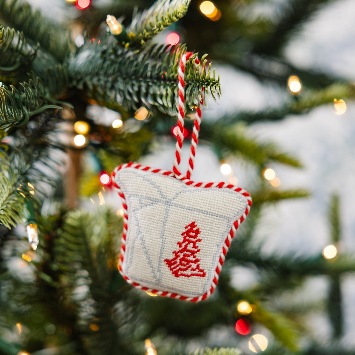 Decorative Christmas ornament with red tree design on a Christmas tree with lights.