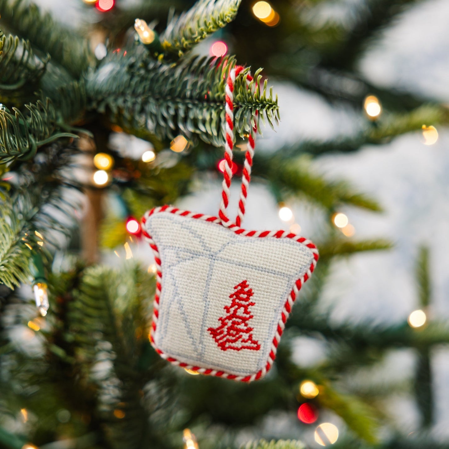 Decorative Christmas ornament with red tree design on a Christmas tree with lights.