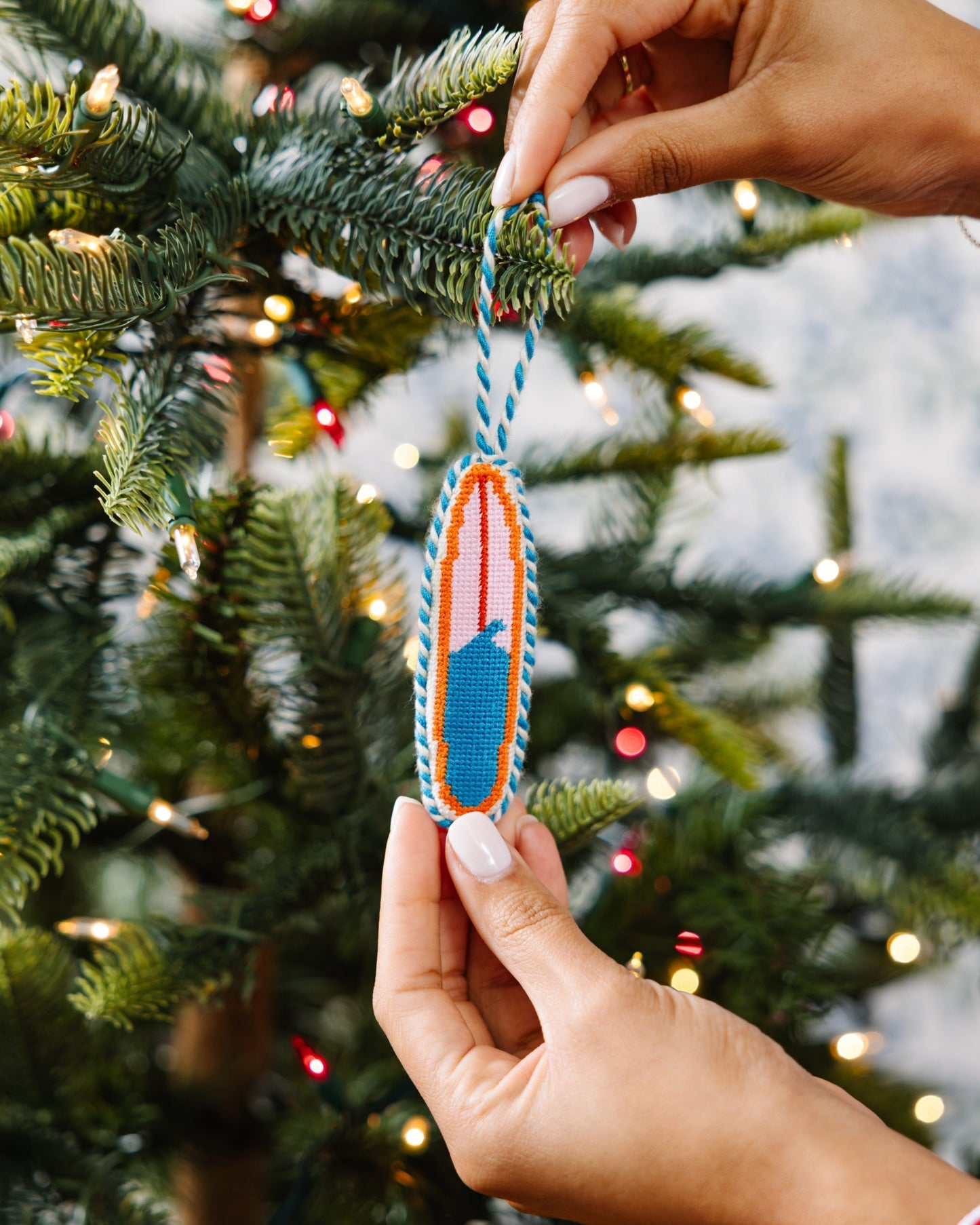 Hand holding a colorful ornament against a Christmas tree background