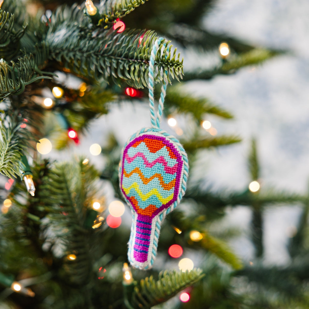 Colorful racket-shaped ornament on a Christmas tree with blurred lights in the background