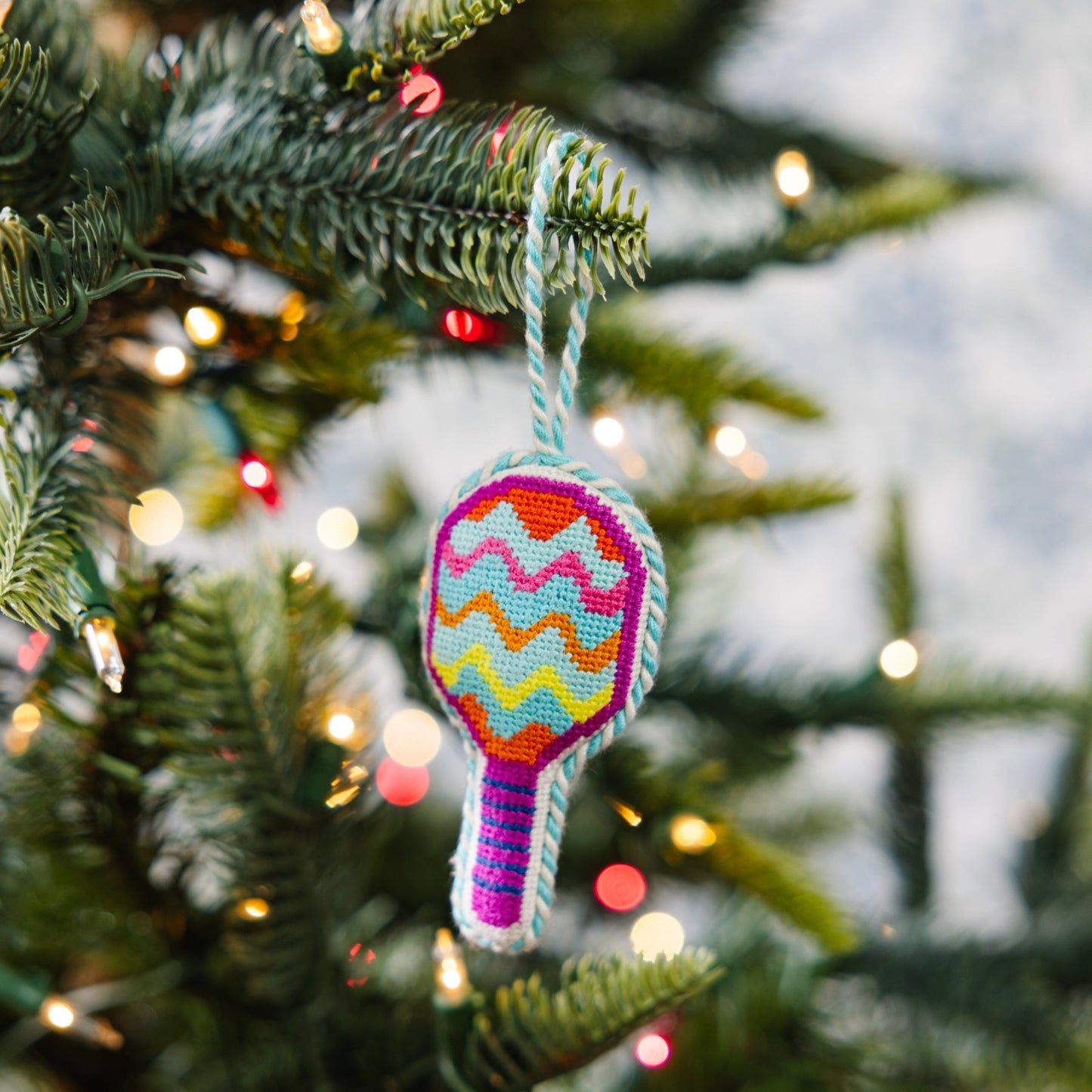 Colorful racket-shaped ornament on a Christmas tree with blurred lights in the background