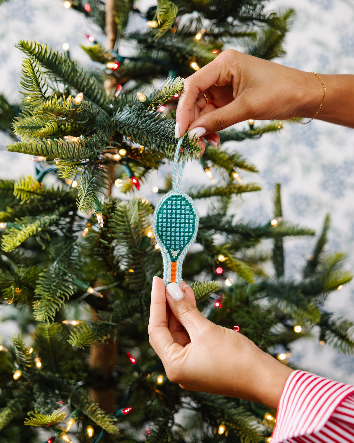 Person decorating a Christmas tree with a decorative ornament.