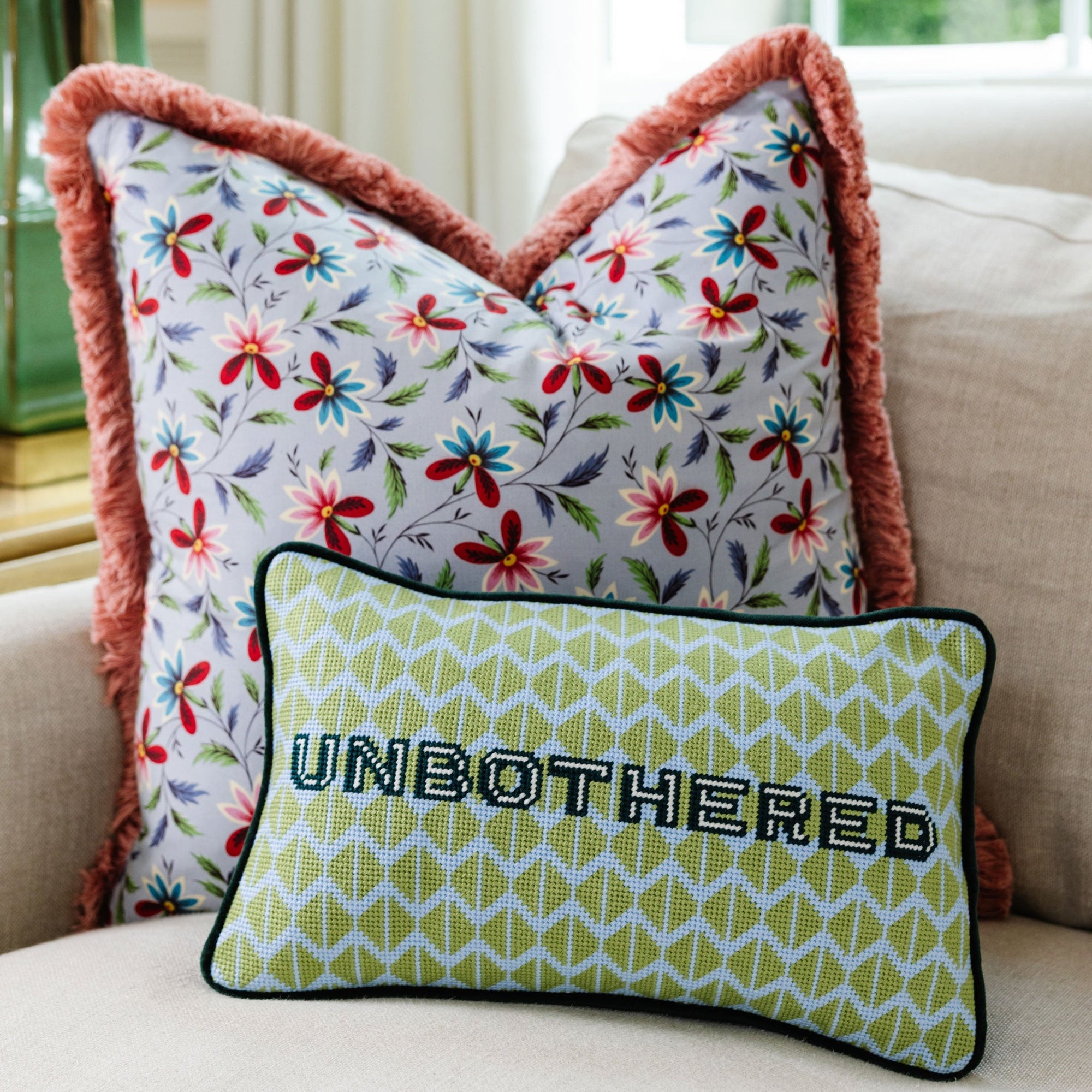 Decorative pillows with floral pattern and 'UNBOtherED' text on a couch.